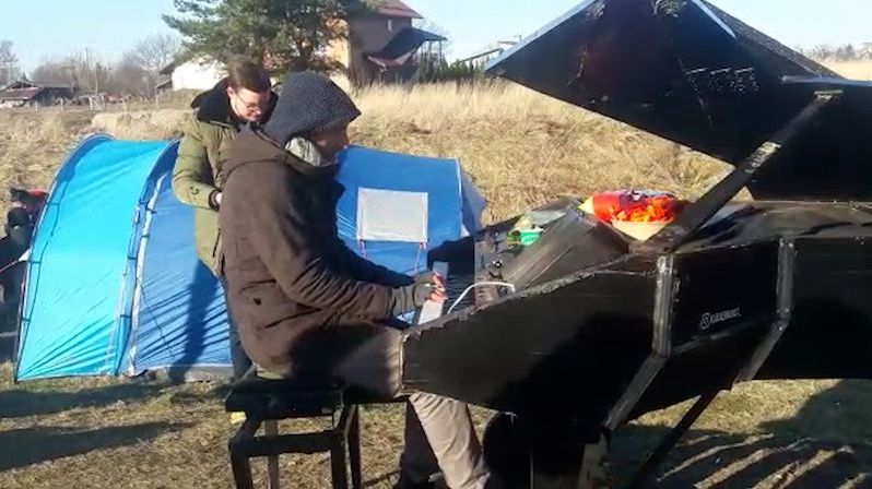 Záblesk radosti: Muž na hranici hrál mezi stany a proudy uprchlíků na piano